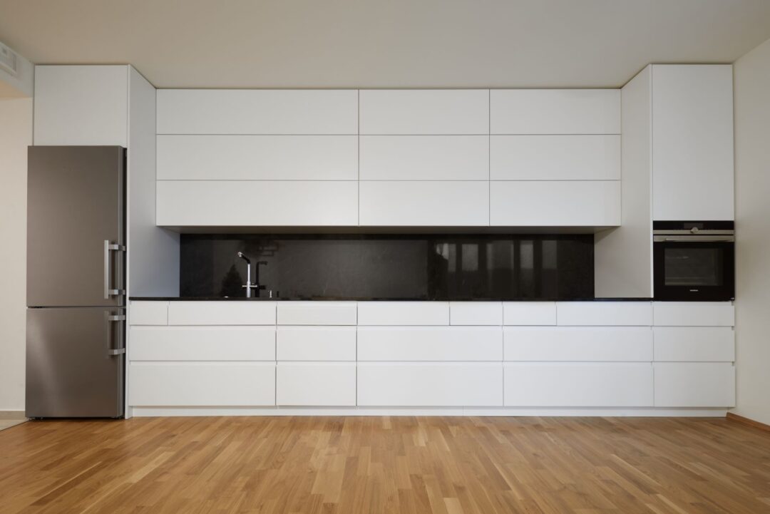 Symetrická bílá kuchyň s kamennou deskou a obkladem