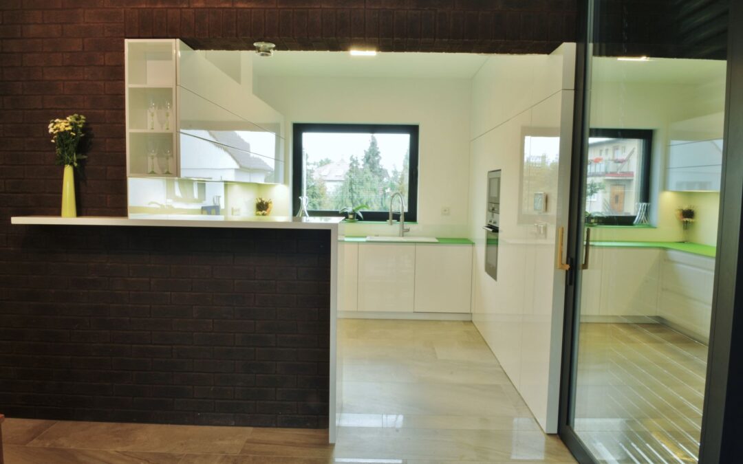 Moderní lakovaná kuchyň, skleněná pracovní deska, obložení stěny se skrytými dveřmi